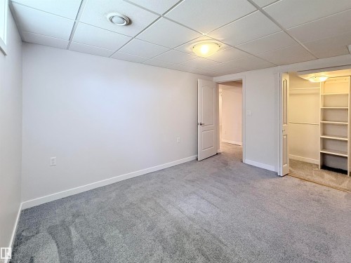 Carpeted room featuring white walls, a drop ceiling, and a built-in closet with shelving - 3912 108 Street, Edmonton, AB - Indoor Photo Showing Other Room