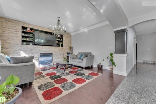 Living area featuring a textured stone-finish accent wall with integrated shelving, a built-in fireplace, and a decorative chandelier - 10915 175 Avenue, Edmonton, AB - Indoor With Fireplace