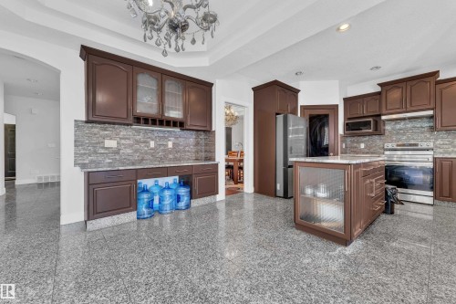 Kitchen featuring dark wood cabinetry, a central island with integrated storage, granite countertops, and a stone-tile backsplash - 10915 175 Avenue, Edmonton, AB - Indoor Photo Showing Kitchen