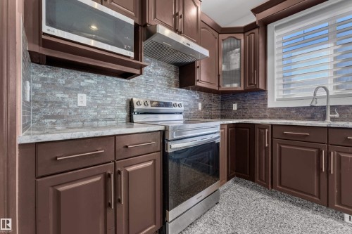 Kitchen featuring dark wood cabinetry, a mosaic tile backsplash, a stainless steel electric range, a stainless steel microwave, and light-toned countertops - 10915 175 Avenue, Edmonton, AB - Indoor Photo Showing Kitchen