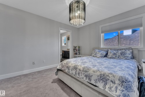 Carpeted room featuring a large window with roller shades, a crystal-style ceiling light fixture, and light gray wall paint - 10915 175 Avenue, Edmonton, AB - Indoor Photo Showing Bedroom