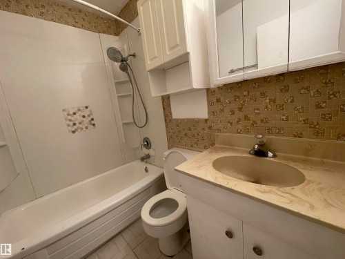 Bathroom featuring a white bathtub and shower combination with a multi-function showerhead, built-in shelving, and a decorative tile accent - 13804 132 Avenue, Edmonton, AB - Indoor Photo Showing Bathroom