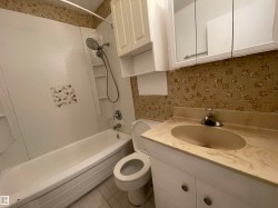 Bathroom featuring a white bathtub and shower combination with a multi-function showerhead, built-in shelving, and a decorative tile accent - 