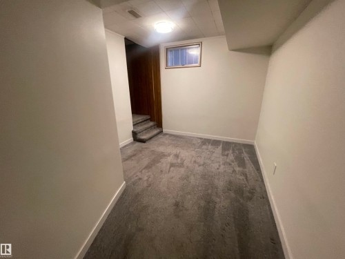 Carpeted room featuring a ceiling-mounted light fixture, a wood-trimmed window, white painted walls, white baseboards, and carpeted stairs with wood-paneled walls - 13804 132 Avenue, Edmonton, AB - Indoor Photo Showing Other Room