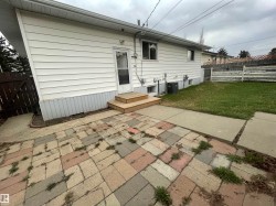Rear exterior featuring white horizontal siding, a wooden privacy fence, a wood stair landing, and a patterned brick patio - 