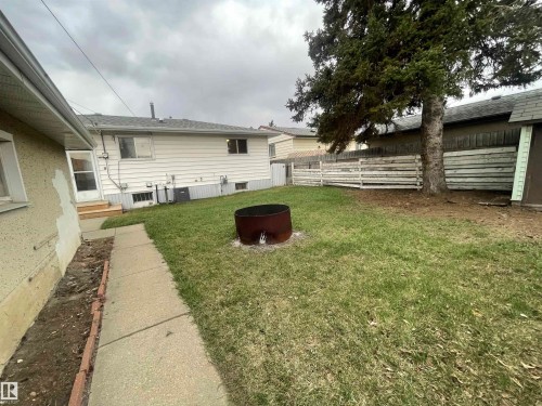Rear yard featuring a concrete walkway, established tree, wood fencing, and a metal fire pit - 13804 132 Avenue, Edmonton, AB - Outdoor
