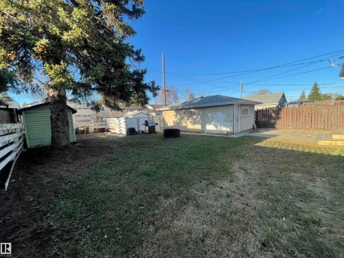 Spacious backyard featuring a detached garage, a green storage shed, mature trees, wood fencing, and a paved patio area - 13804 132 Avenue, Edmonton, AB - Outdoor