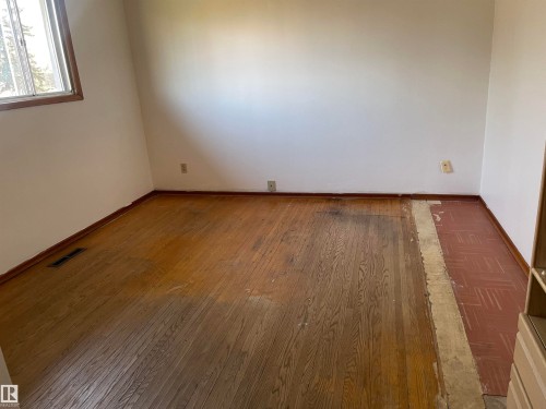 Wood-finish flooring with a partially exposed subfloor, white painted walls, and a single window with wood trim - 13804 132 Avenue, Edmonton, AB - Indoor Photo Showing Other Room