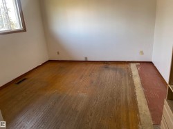 Wood-finish flooring with a partially exposed subfloor, white painted walls, and a single window with wood trim - 