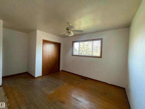 Room featuring wood-finish flooring, a ceiling fan, a window with wood trim, and a built-in closet with sliding wood doors - 13804 132 Avenue, Edmonton, AB - Indoor Photo Showing Other Room