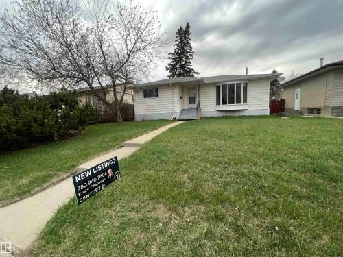 White siding exterior with a prominent bay window, front entrance with steps, concrete walkway, and a landscaped front yard with grass and mature shrubbery - 13804 132 Avenue, Edmonton, AB - Outdoor