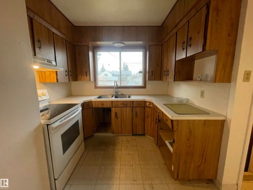 Kitchen featuring wood-finish cabinetry, white countertops, and a double-basin stainless steel sink with a window above - 13804 132 Avenue, Edmonton, AB - Indoor Photo Showing Kitchen With Double Sink