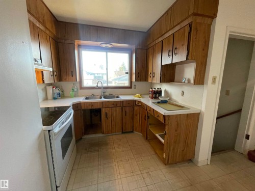 Kitchen with L-shaped wood-finish cabinetry, white countertops, and a double-basin stainless steel sink - 13804 132 Avenue, Edmonton, AB - Indoor Photo Showing Kitchen With Double Sink