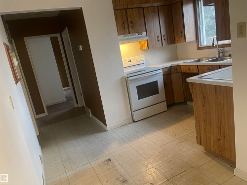 Kitchen featuring wood-finish cabinetry, white countertops, a double basin sink with window, and a white electric range with matching hood - 13804 132 Avenue, Edmonton, AB - Indoor Photo Showing Kitchen With Double Sink