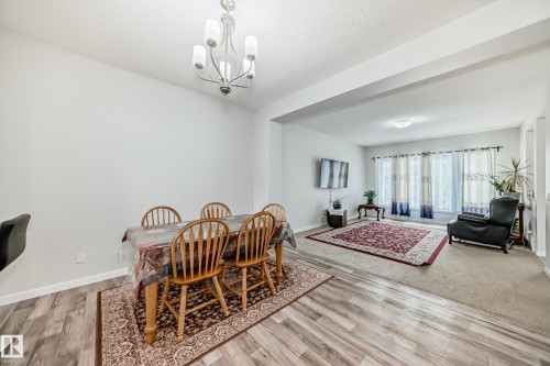 Open-concept living space featuring wood-finish flooring, a contemporary chandelier, and a broad entry point to the carpeted living area - 4609 Alwood Way, Edmonton, AB - Indoor