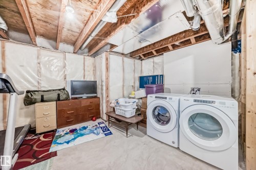 Dedicated laundry area featuring a front-loading washer and dryer, exposed ceiling joists, and visible insulation - 4609 Alwood Way, Edmonton, AB - Indoor Photo Showing Laundry Room