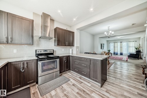 Contemporary kitchen featuring wood-finish cabinetry, light-toned countertops, and a stainless steel appliance suite with a matching range hood - 4609 Alwood Way, Edmonton, AB - Indoor Photo Showing Kitchen With Upgraded Kitchen