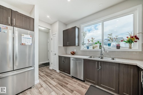 Kitchen featuring wood-finish flooring, dark wood-finish cabinetry with silver hardware, light-toned countertops, and a white subway tile backsplash - 4609 Alwood Way, Edmonton, AB - Indoor Photo Showing Kitchen With Stainless Steel Kitchen With Double Sink