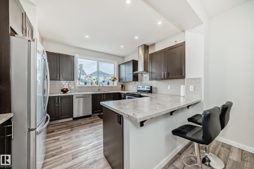 Contemporary kitchen featuring wood-finish flooring, dark wood cabinetry, stainless steel appliances, a light-toned countertop, and a tiled backsplash - 4609 Alwood Way, Edmonton, AB - Indoor Photo Showing Kitchen
