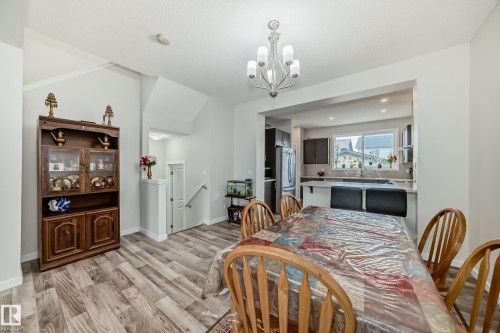 Dining area featuring wood-finish flooring, a contemporary chandelier, and an open pass-through to the kitchen with a breakfast bar - 4609 Alwood Way, Edmonton, AB - Indoor Photo Showing Dining Room