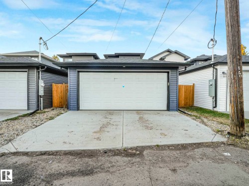 Detached garage featuring a white overhead door, gray siding, a dark shingle roof, and an adjacent concrete pad - 15731 109 Avenue, Edmonton, AB - Outdoor With Exterior