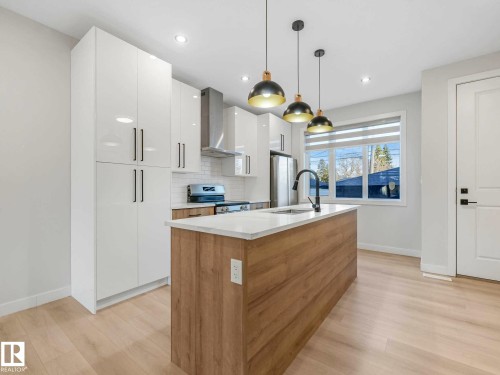 Contemporary kitchen featuring a light wood-finish island with integrated sink, white flat-panel cabinetry, stainless steel appliances, and light wood-finish flooring - 15731 109 Avenue, Edmonton, AB - Indoor Photo Showing Kitchen With Upgraded Kitchen