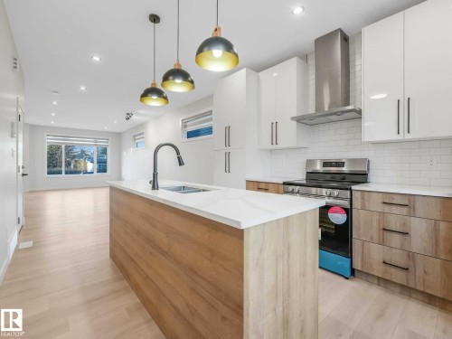 Modern kitchen featuring a central island with an integrated sink, three pendant lights, stainless steel appliances, and wood-finish cabinetry - 15731 109 Avenue, Edmonton, AB - Indoor Photo Showing Kitchen With Double Sink With Upgraded Kitchen