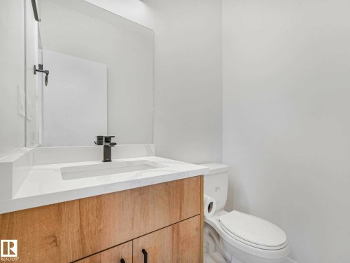 Powder room featuring a wood-finish vanity with a white countertop, an integrated sink, and a modern black faucet - 15731 109 Avenue, Edmonton, AB - Indoor Photo Showing Bathroom