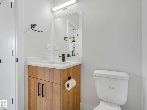 Modern bathroom featuring a wood-finish vanity with matte black hardware, white countertop, rectangular undermount sink, and a black single-handle faucet - 15731 109 Avenue, Edmonton, AB - Indoor Photo Showing Bathroom