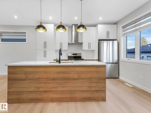 Modern kitchen featuring a central island with wood-finish paneling, light countertop, and integrated sink with a matte black faucet - 15731 109 Avenue, Edmonton, AB - Indoor Photo Showing Kitchen With Double Sink With Upgraded Kitchen