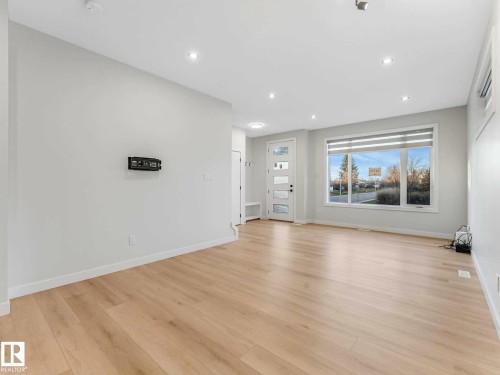 Spacious interior featuring light wood-finish flooring, recessed lighting, and a large front-facing window - 15731 109 Avenue, Edmonton, AB - Indoor