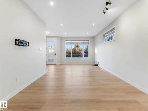 Spacious room featuring light wood-finish flooring, recessed lighting, and a modern white entry door with frosted glass panels - 15731 109 Avenue, Edmonton, AB - Indoor Photo Showing Living Room