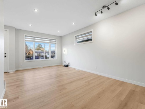 Spacious room featuring light wood-finish flooring, recessed lighting, and a large multi-pane window - 15731 109 Avenue, Edmonton, AB - Indoor