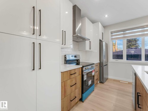 Modern kitchen featuring white high-gloss cabinetry, stainless steel appliances, light wood-finish lower cabinets, white subway tile backsplash, and light wood-finish flooring - 15731 109 Avenue, Edmonton, AB - Indoor Photo Showing Kitchen With Upgraded Kitchen