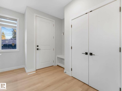 Foyer entrance featuring light wood-finish flooring, a white paneled door with dark hardware, and double white closet doors with dark hardware - 15731 109 Avenue, Edmonton, AB - Indoor Photo Showing Other Room