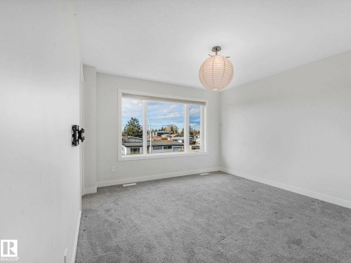 Bright interior space featuring a large window, light-colored walls, gray carpet, white trim, and a spherical ceiling light fixture - 15731 109 Avenue, Edmonton, AB - Indoor Photo Showing Other Room