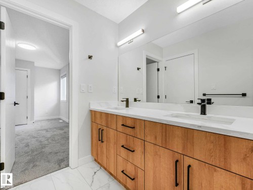Dual vanity featuring wood-finish cabinetry, a white countertop with integrated sinks, and matte black fixtures - 15731 109 Avenue, Edmonton, AB - Indoor Photo Showing Bathroom
