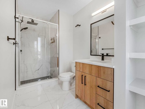 Bathroom featuring a glass-enclosed shower with a rainfall showerhead, a wood-finish vanity with a white countertop, a black-framed mirror, and a toilet - 15731 109 Avenue, Edmonton, AB - Indoor Photo Showing Bathroom