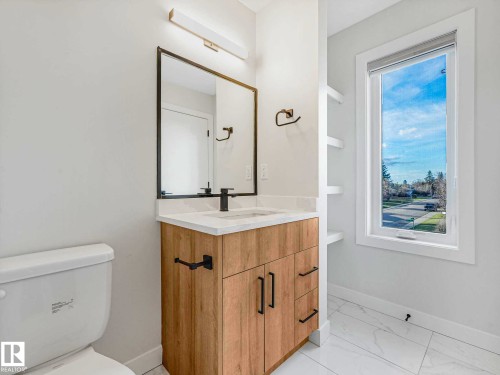 Bathroom featuring a wood-finish vanity with an integrated sink and matte black faucet, a large framed mirror, built-in shelving, white tile flooring, and a window with white trim - 15731 109 Avenue, Edmonton, AB - Indoor Photo Showing Bathroom