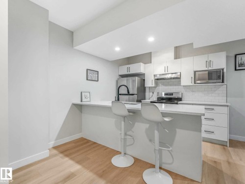 Kitchen featuring light wood-finish flooring, white cabinetry, stainless steel appliances, a subway tile backsplash, and a breakfast bar - 15731 109 Avenue, Edmonton, AB - Indoor Photo Showing Kitchen With Upgraded Kitchen