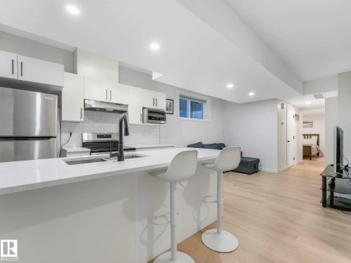 Modern kitchen featuring stainless steel appliances, white cabinetry, a subway tile backsplash, and a large island with an undermount sink - 15731 109 Avenue, Edmonton, AB - Indoor Photo Showing Kitchen
