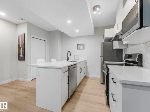 Contemporary kitchen featuring a center island with sink, white cabinetry, integrated stainless steel appliances, light wood-finish flooring, and white subway tile backsplash - 15731 109 Avenue, Edmonton, AB - Indoor Photo Showing Kitchen