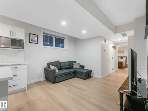 Open-concept living area featuring light wood-finish flooring, recessed lighting, and a kitchen area with white cabinetry, a built-in microwave, and subway tile backsplash - 15731 109 Avenue, Edmonton, AB - Indoor