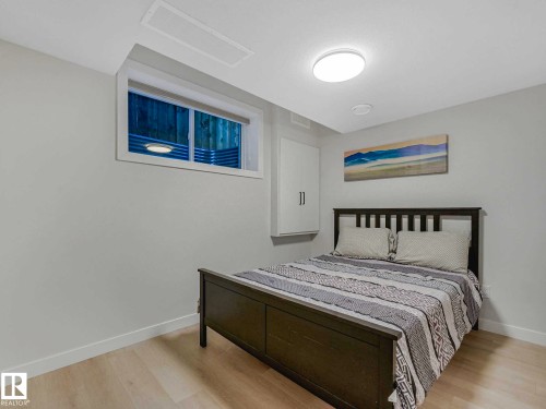 Well-lit room featuring light wood-finish flooring, a white trim baseboard, and a built-in wall cabinet with double doors - 15731 109 Avenue, Edmonton, AB - Indoor Photo Showing Bedroom