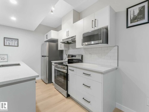 Modern kitchen featuring light wood-finish flooring, white cabinetry with dark hardware, stainless steel appliances, and white subway tile backsplash - 15731 109 Avenue, Edmonton, AB - Indoor Photo Showing Kitchen