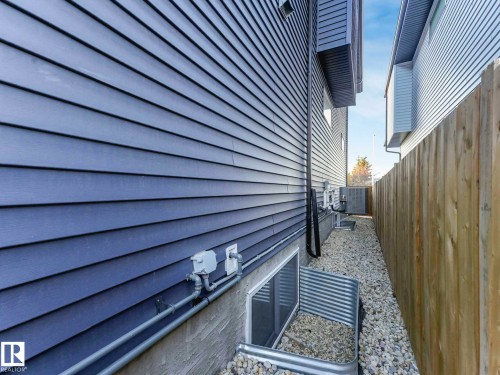 Siding exterior with horizontal panels, gravel landscaping, a window well, a wooden fence, and visible utility lines - 15731 109 Avenue, Edmonton, AB - Outdoor