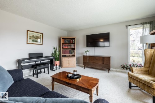 Spacious living area featuring light-toned carpeting, a large wall-mounted display, and a window with natural light - 3608 16A Avenue, Edmonton, AB - Indoor Photo Showing Living Room