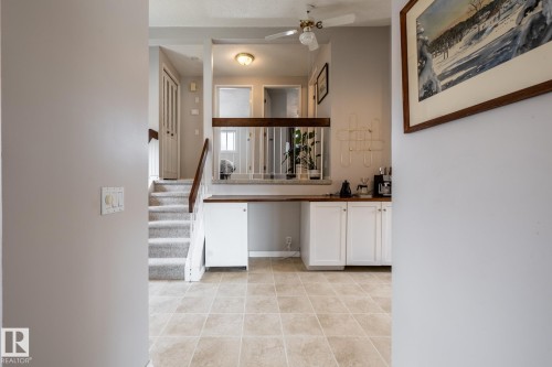 Multi-level interior featuring tile flooring, a carpeted staircase with wood handrails, a ceiling fan, and white cabinetry with a wood-finish countertop - 3608 16A Avenue, Edmonton, AB - Indoor Photo Showing Other Room