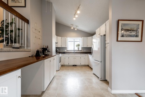 Kitchen featuring white cabinetry, dark countertops, a window over the sink, and white appliances - 3608 16A Avenue, Edmonton, AB - Indoor Photo Showing Kitchen