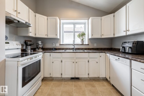 Kitchen with white cabinetry, dark stone-finish countertops, and a double basin sink beneath a window - 3608 16A Avenue, Edmonton, AB - Indoor Photo Showing Kitchen With Double Sink